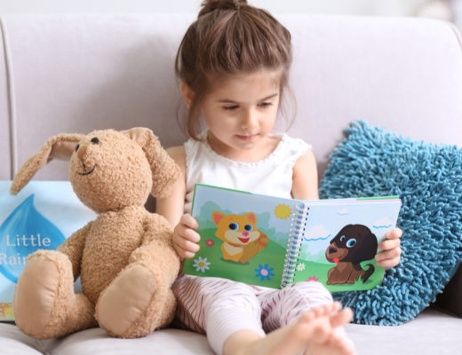little girl reading a book with a stuffed animal